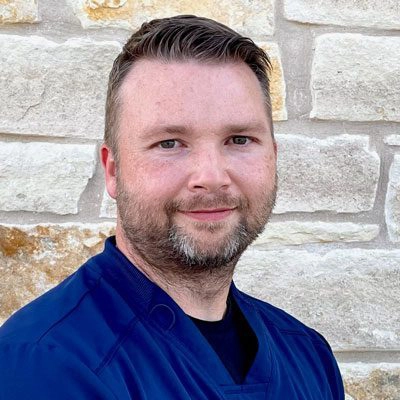 Adam Jester smiling in front of a stone wall.