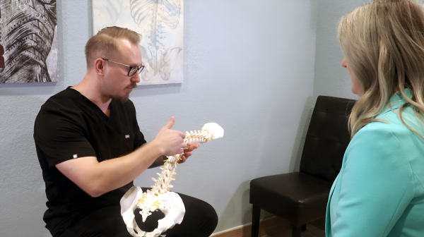 Andrew Yakubik giving a patient a consultation. He is holding a spine.