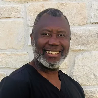 Roland Njumentoko smiling in front of a stone wall.
