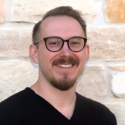 Andrew Yakubik smiling in front of a stone wall.