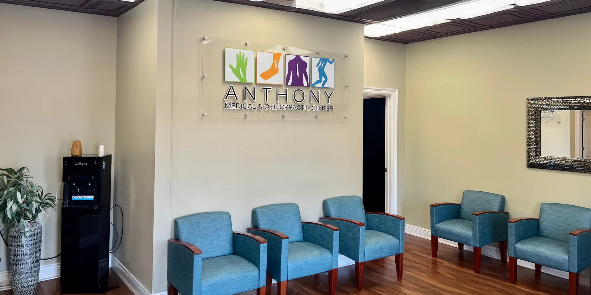 The inside of the clinic. There is a Anthony Medical & Chiropractic Center sign above the blue waiting room chairs.