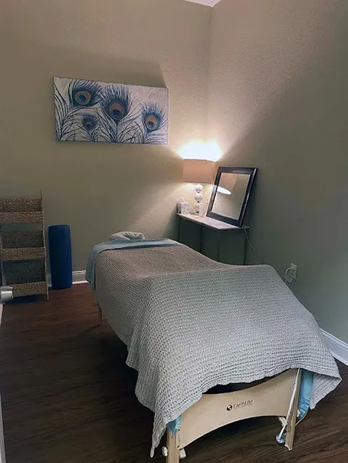 A massage room with a table. The room has a picture of peacock feathers.