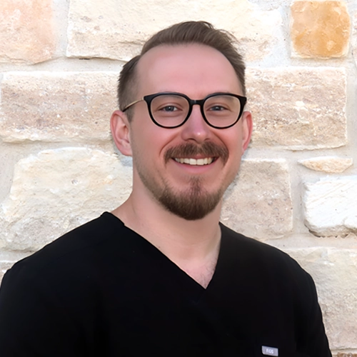 Andrew Yakubik smiling in front of a stone wall.