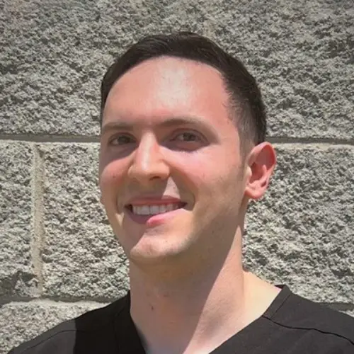 Brandon Asher smiling in front of a stone wall.