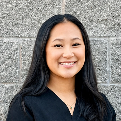 Trinh Nguyen, D.C., M.B.A. smiling in front of a brick wall.