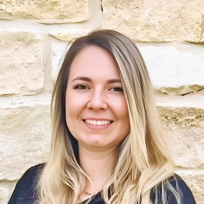 Angela Krego smiling in front of a stone wall.