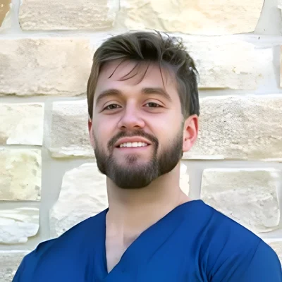Matthew Grenda smiling in front of a brick wall.